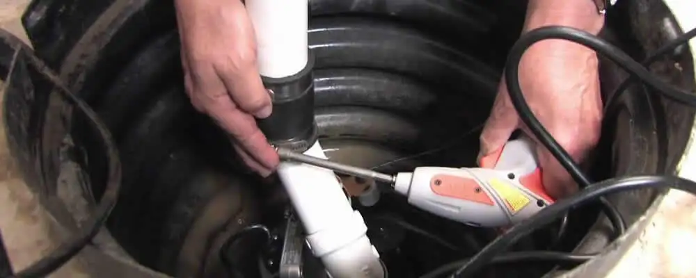 Sump pump installation technician connecting PVC discharge piping in Boston, MA