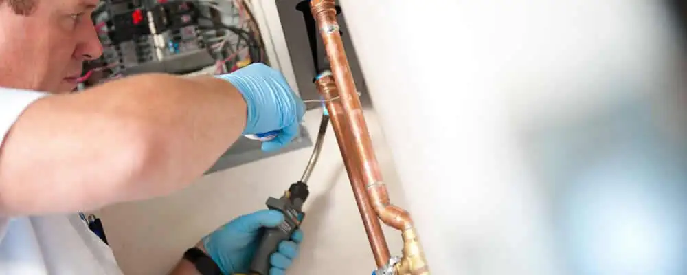 Water heater repair technician testing copper pipe connections and controls in Boston, MA